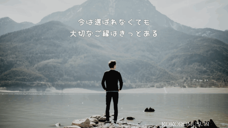 婚活で選ばれない男性が、湖畔に立ち遠くの山を見つめている後ろ姿。「今は選ばれなくても 大切なご縁はきっとある」という前向きなメッセージとKOKOROMUSUBIのロゴ入り。